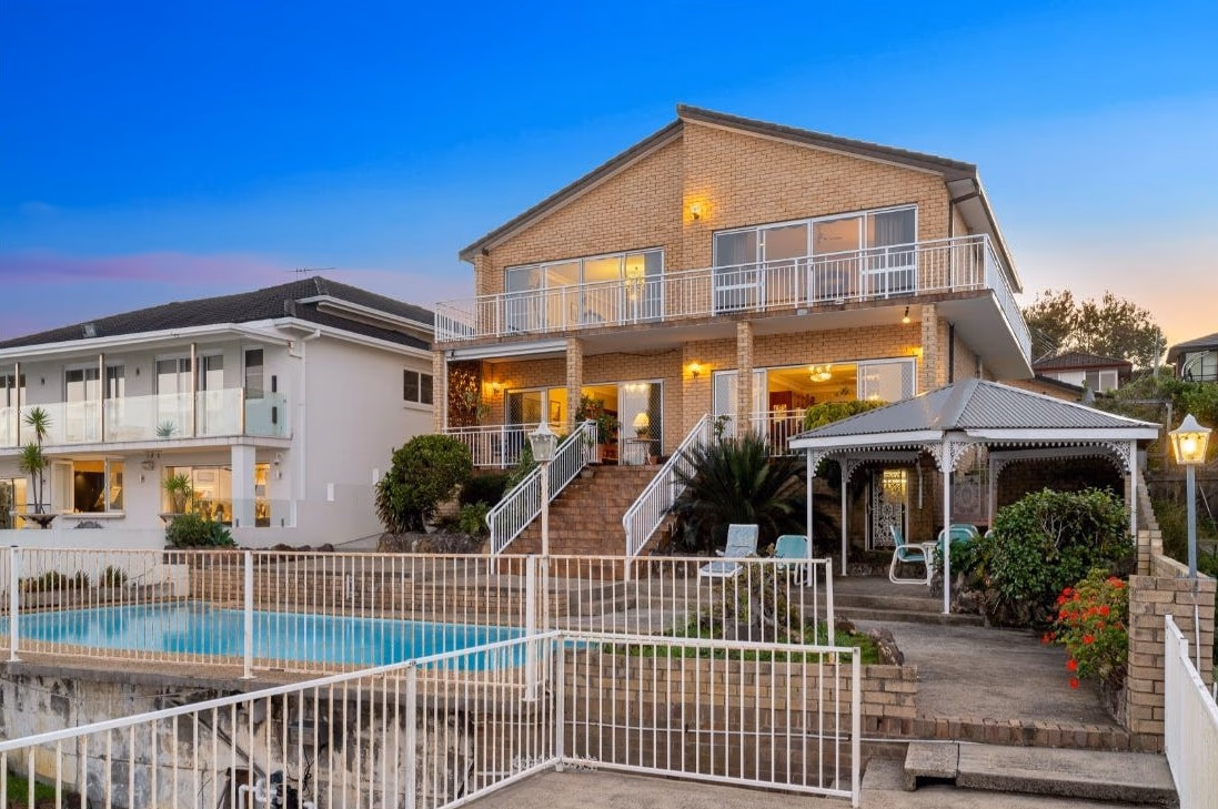 Two-storey brick waterfront home with pool and gazebo at dusk
