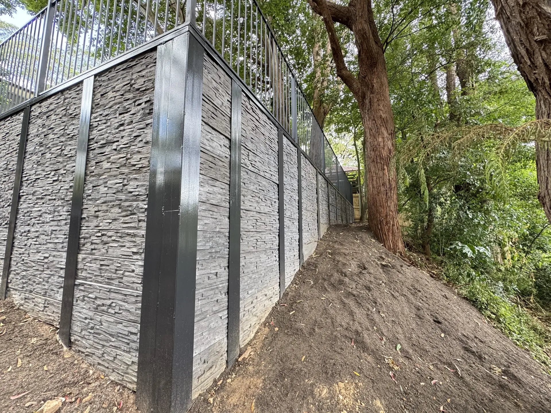 Stone-clad retaining wall built by IA Engineering along a sloped site
