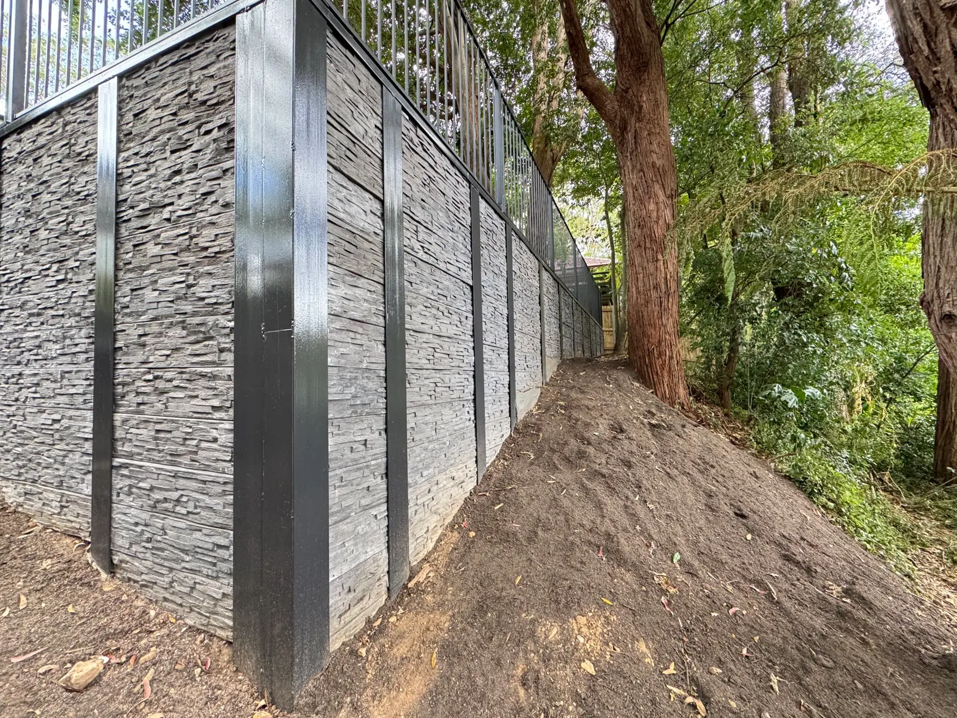 Stone-clad retaining wall built by IA Engineering along a sloped, tree-lined site